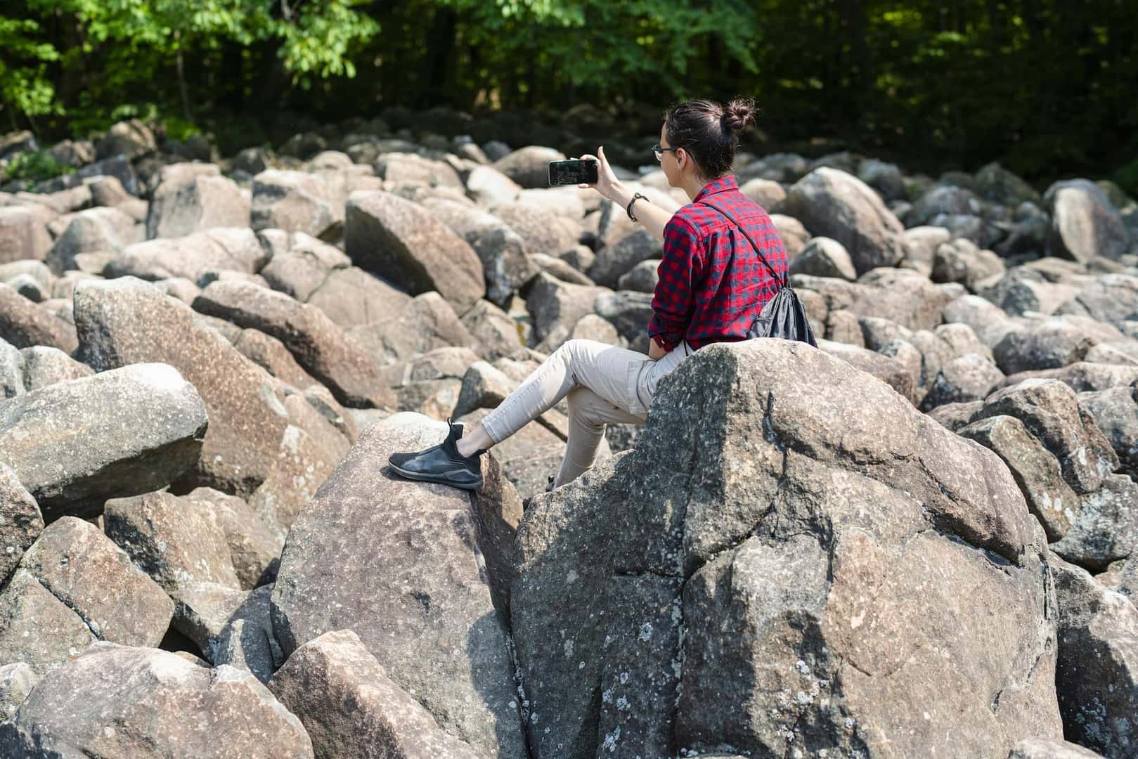 Teenage girl taking a mobile photo when she is explore boulder field in Poconos, Pennsylvania, USA, on a sunny summerday.