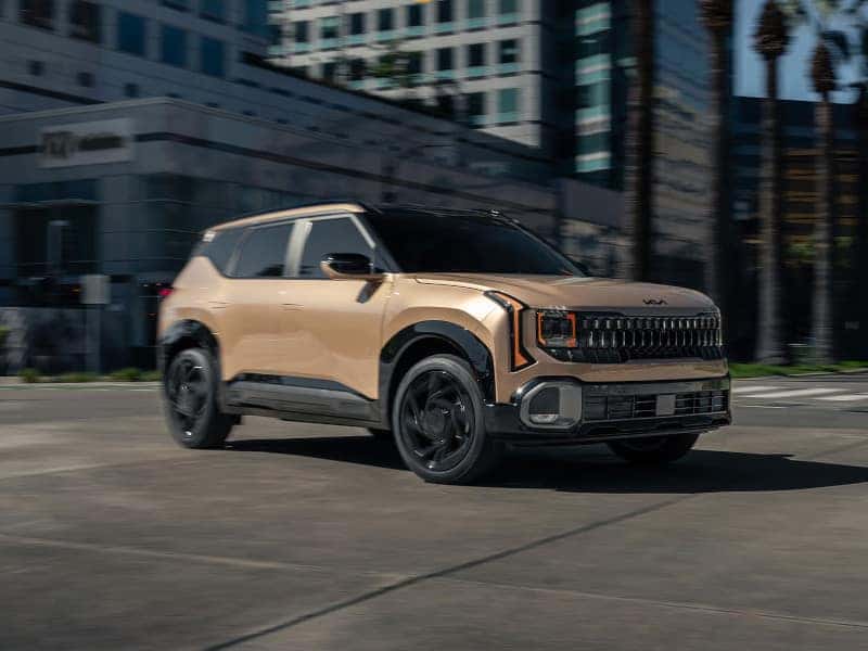 A sleek, beige SUV with black accents drives on an urban street. Tall buildings and palm trees in the background convey a modern, vibrant city vibe.