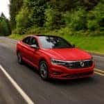 A red 2021 Volkswagen Jetta is driving on a tree-lined road after leaving a VW dealer near me.