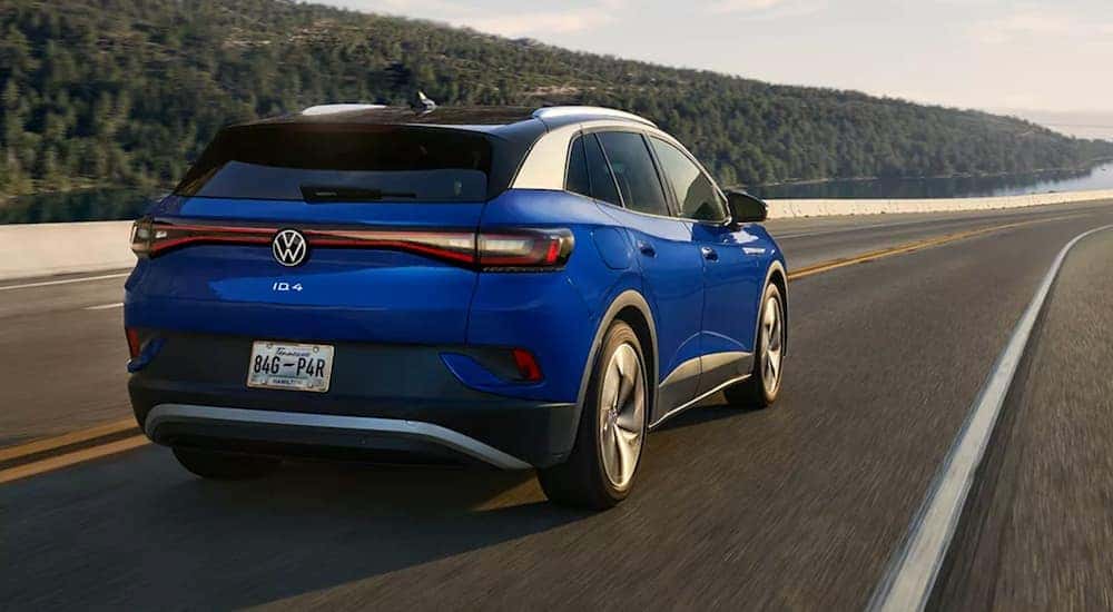 A blue Volkswagen ID.4 is shown from the rear driving toward a lake.