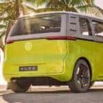 Three people are standing near a lime green Volkswagen ID.BUZZ concept van at the beach.