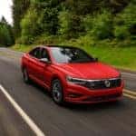 A red 2021 Volkswagen Jetta R-line is show driving down a tree lined road after leaving a VW Jetta dealer in Seattle.