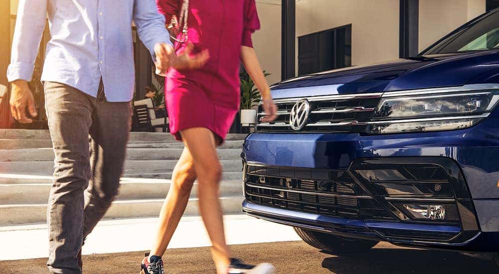 A couple is shown walking past the front of a blue 2021 Volkswagen Tiguan R-Line.