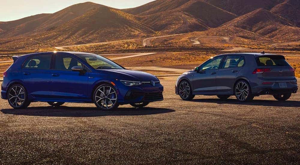 A blue 2022 Volkswagen Golf R and a grey Golf GTI are shown parked on tarmac.