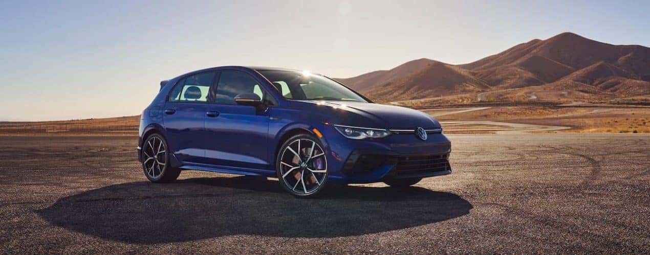 A blue 2022 Volkswagen Golf R is shown from the side parked in an open desert lot.