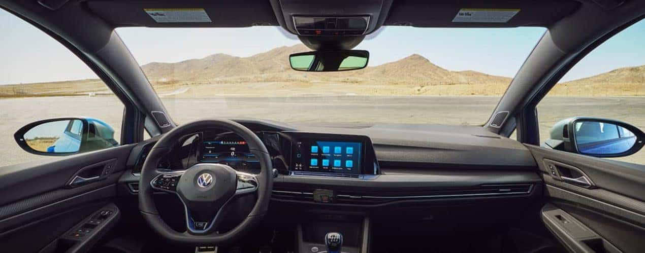 The black interior of a 2022 Volkswagen Golf R shows the steering wheel and infotainment screen.