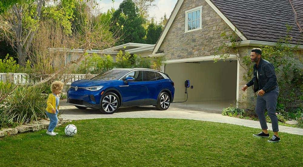 A blue 2021 Volkswagen ID.4 is shown charging while a girl plays soccer on a lawn.