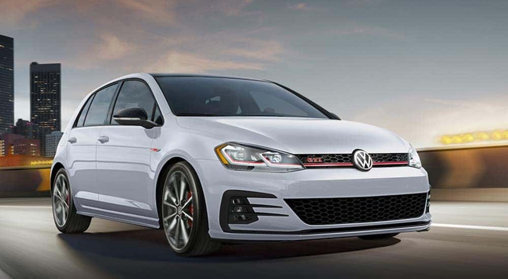 A white 2021 Volkswagen Golf GTI is shown driving on bridge leaving a city.