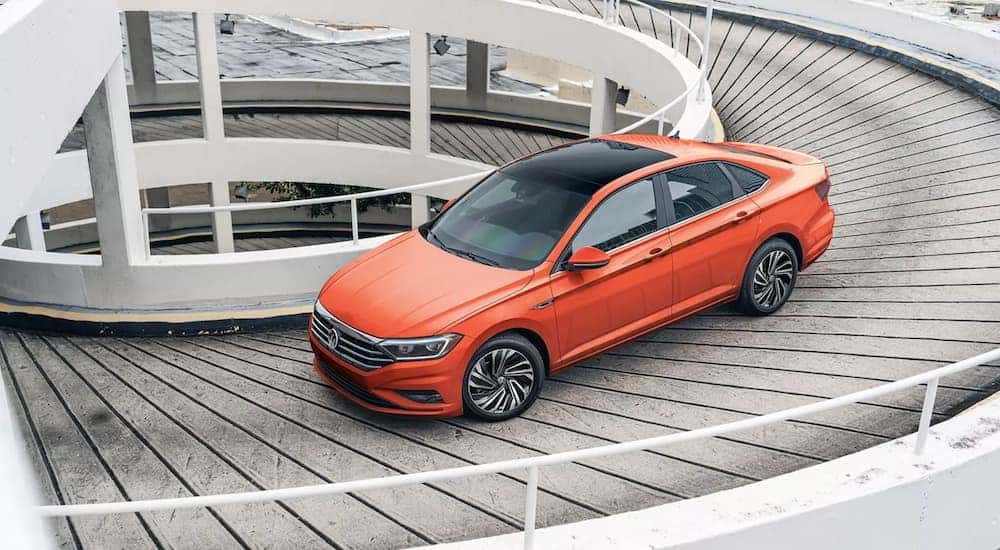 An orange 2021 Volkswagen Jetta is shown driving down a spiral parking garage exit.