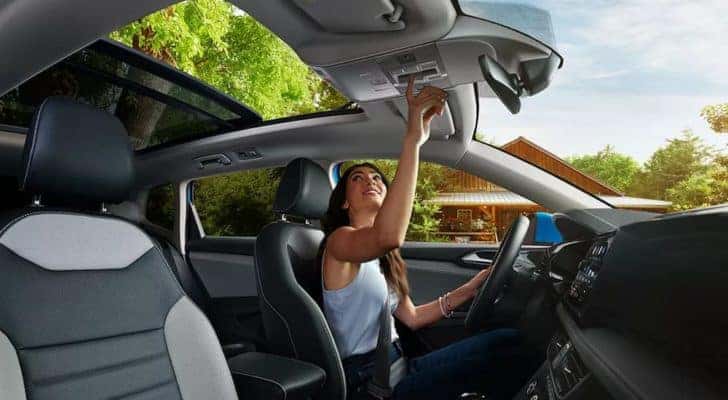 A woman is shown opening the moonroof of a blue 2022 Volkswagen Taos.