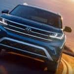 A blue 2022 Volkswagen Atlas is shown driving on a road away from the ocean.