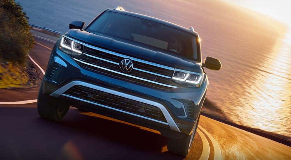 A blue 2022 Volkswagen Atlas is shown driving on a road away from the ocean.