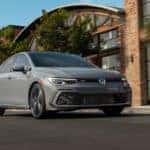 A grey 2022 Volkswagen Golf GTI is shown from the front driving in front of a modern building after leaving a Seattle VW GTI dealer.