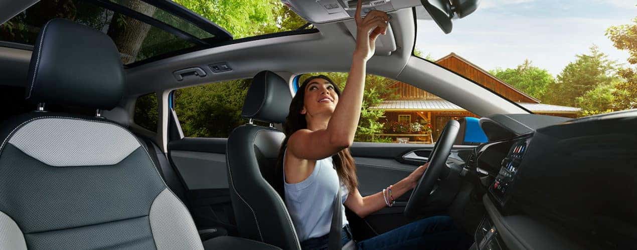 A woman is shown opening the sunroof in a 2022 Volkswagen Taos.