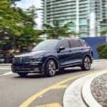 A popular used Volkswagen for sale, a dark blue 2018 Volkswagen Tiguan, is shown driving in a city.