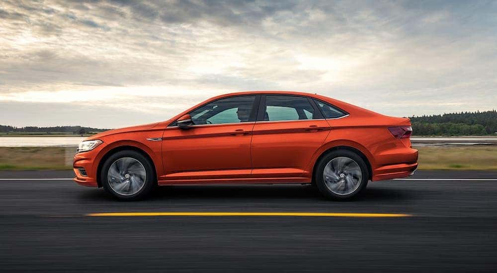 An orange 2022 Volkswagen Jetta is shown from the side driving on an open road.
