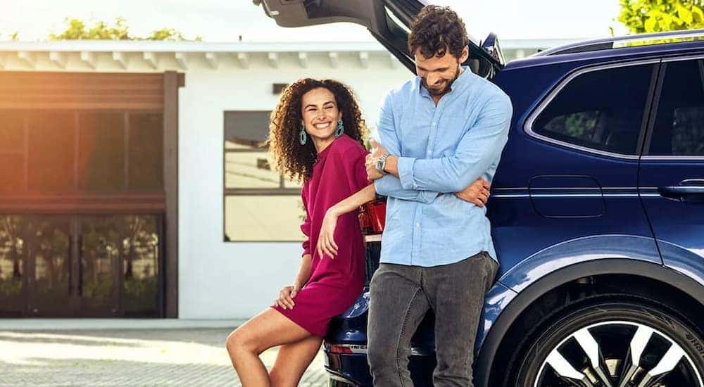 A couple is shown leaning up against a blue 2021 Volkswagen Tiguan.
