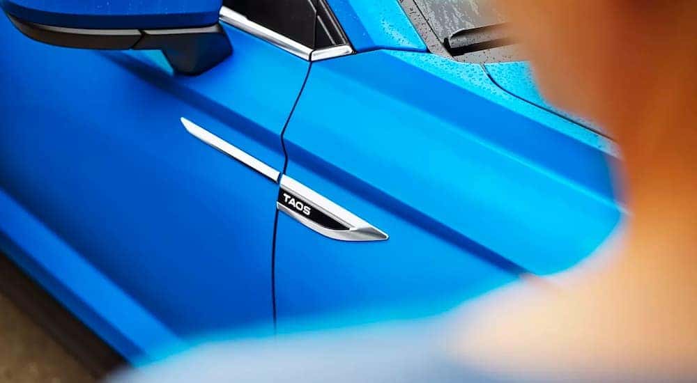 A close up shows the Taos badge on the door or a blue 2023 Volkswagen Taos.