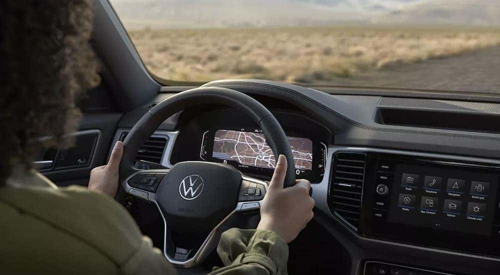 The black interior of a 2023 Volkswagen Atlas Cross Sport SEL shows the steering wheel and infotainment screen.