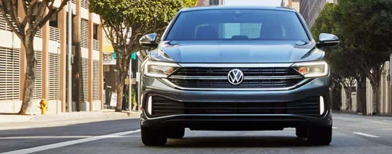 A grey 2023 Volkswagen Jetta is shown from the front driving on a city street.