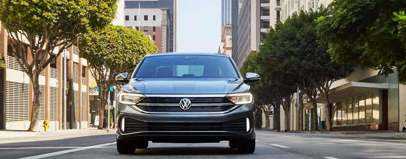 A grey 2023 Volkswagen Jetta SEL is shown from the front driving on a city street.