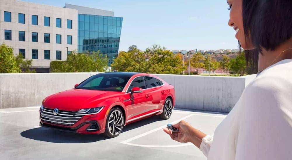 Someone is shown locking a red 2023 Volkswagen Arteon with a key fob.