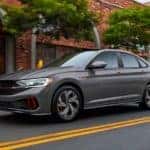 A grey 2023 Volkswagen Jetta GLI Autobahn is shown driving on a city street.