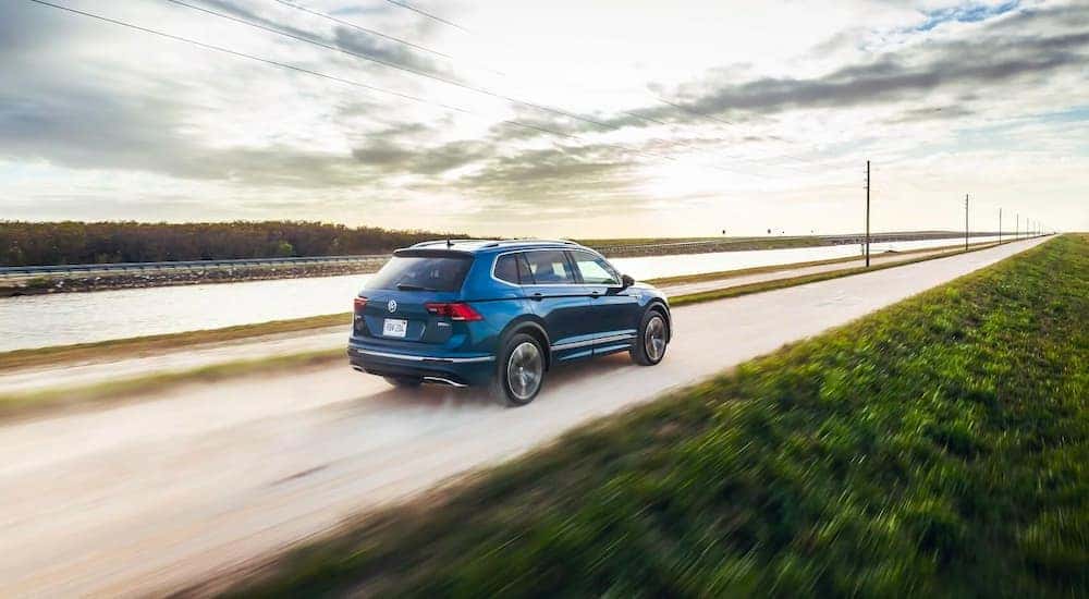 A blue 2021 Volkswagen Tiguan is shown driving on a path on a cloudy day.