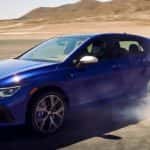 A blue 2023 Volkswagen Golf R is shown driving on an open desert area.