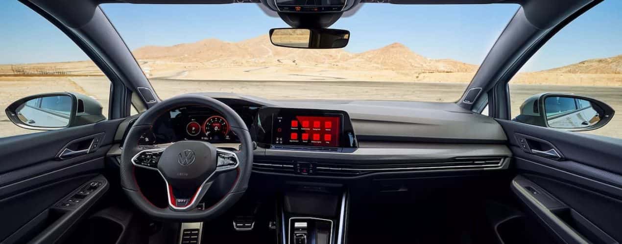 The black dashboard and steering wheel in a 2023 Volkswagen Golf GTI is shown during a 2023 Volkswagen Golf R vs 2023 Volkswagen Golf GTI comparison.