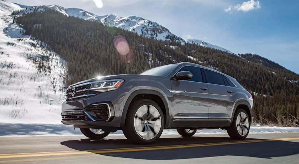 A gray 2023 Volkswagen Atlas Cross Sport is shown driving near a mountain.