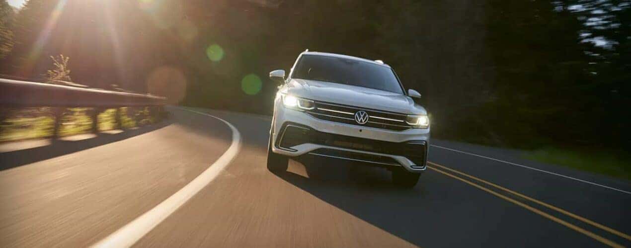 A white 2023 Volkswagen Tiguan is shown from the front driving on a winding road.