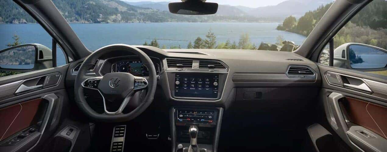 The black and grey interior of a 2023 Volkswagen Tiguan shows the steering wheel and center console.