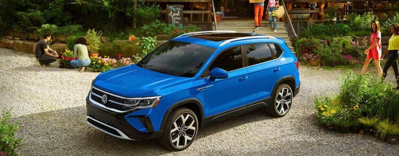 A blue 2023 Volkswagen Taos is shown parked outside of a flower shop.