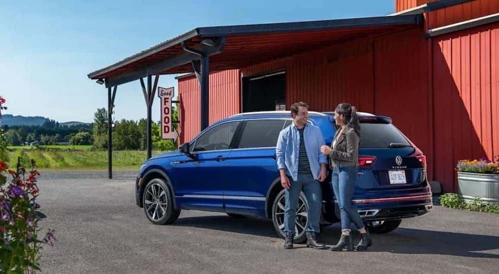 A blue 2023 Volkswagen Tiguan is shown parked near a red building.