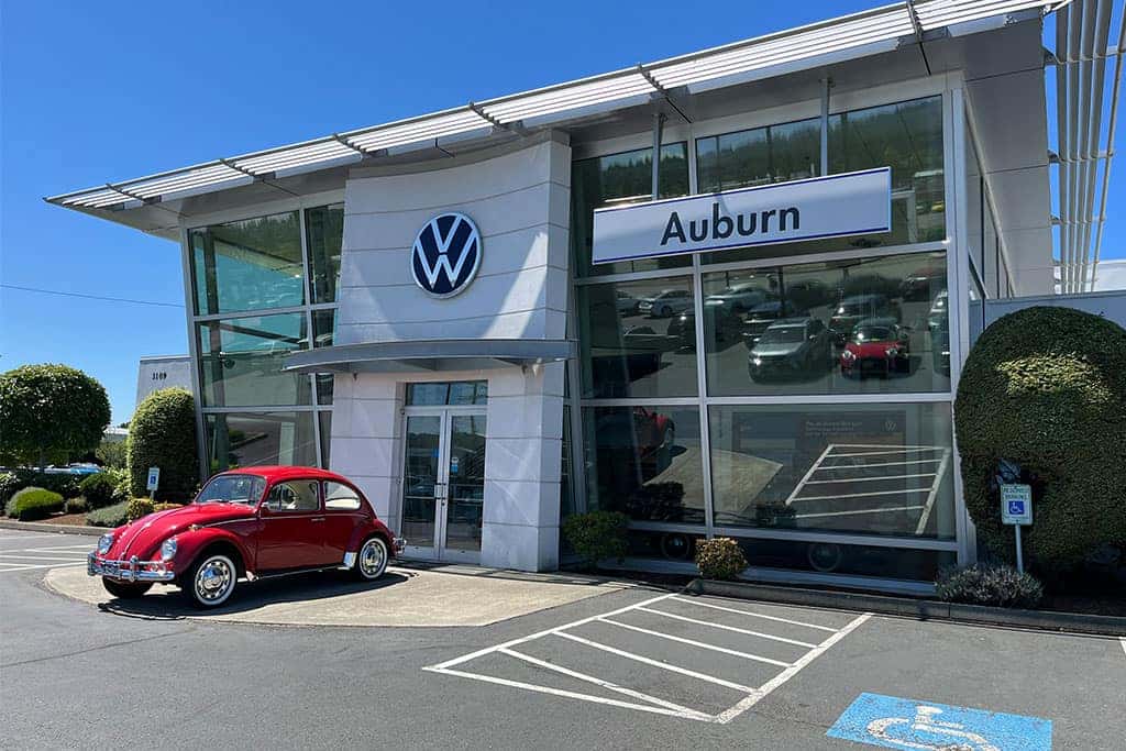 Front entrance of Bud Clary Auburn VW with a vintage VW Beetle parked outside