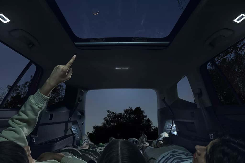 3 people laying down in the back of a 2026 VW Atlas looking up at the stars through the panoramic sunroof