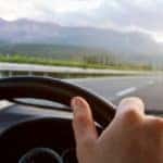 Hands on a steering wheel driving car down the road