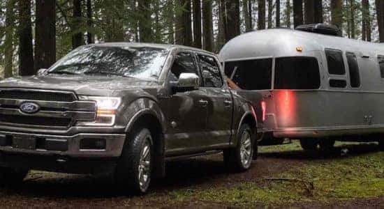 Silver Ford F-150 towing a trailer in the woods