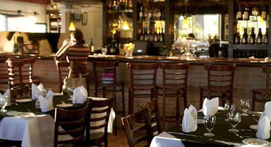 Interior shot of tables at a restaurant with a bar in the background.