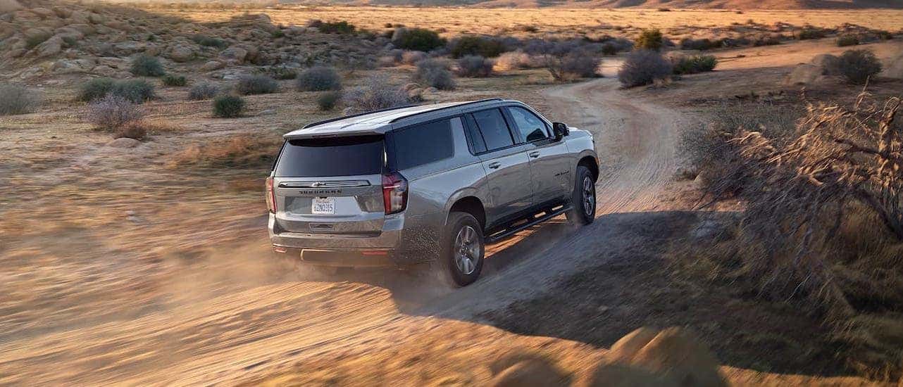 A gray 2021 Chevy Suburban is driving on a dirt road in the desert.