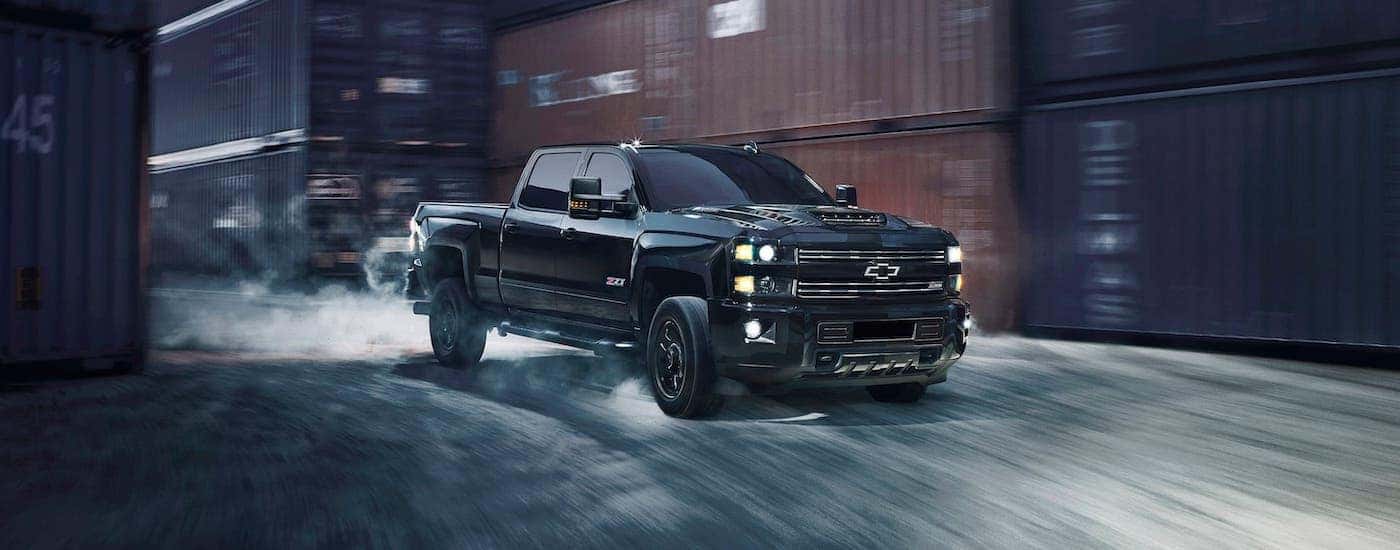 A black 2017 used Chevy Silverado 2500HD Z71 is driving past shipping containers.