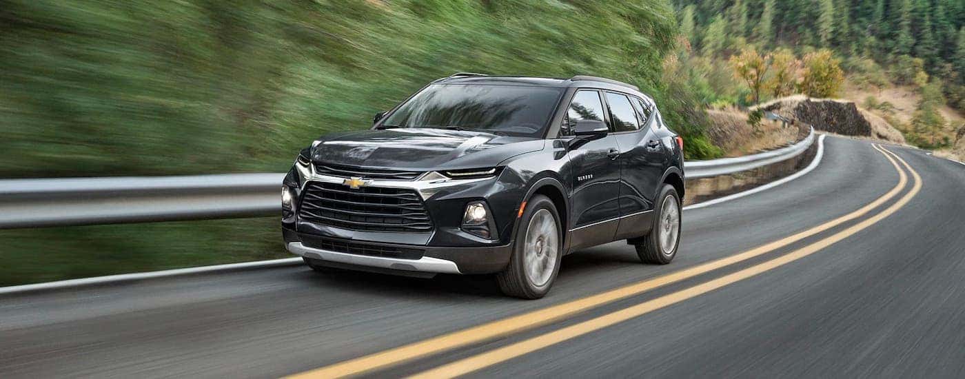 A black 2021 Chevy Blazer is driving on a winding road past trees.