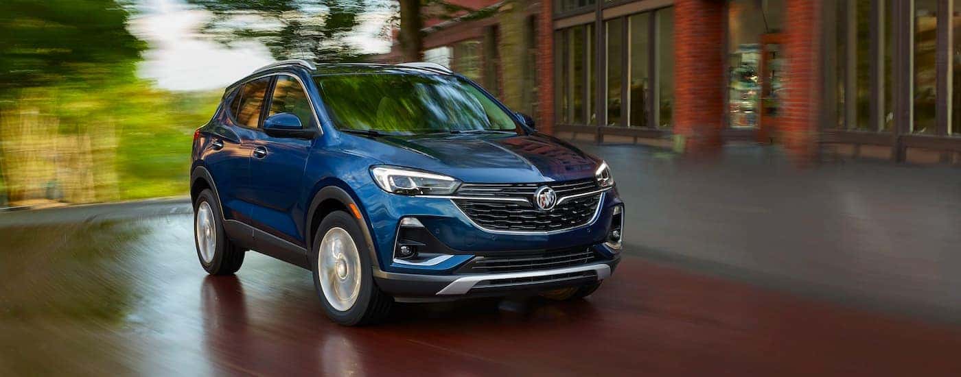 A blue 2021 Buick Encore GX is shown driving past a blurred building and trees.