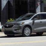 A grey 2021 Buick Enclave is parked on a city street next to a family eating outside.