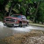 A popular pre-owned Chevy truck, a burgundy 2014 Chevy Silverado LTZ, is driving through a stream.