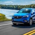 A blue 2018 Buick Encore is driving past a lake.