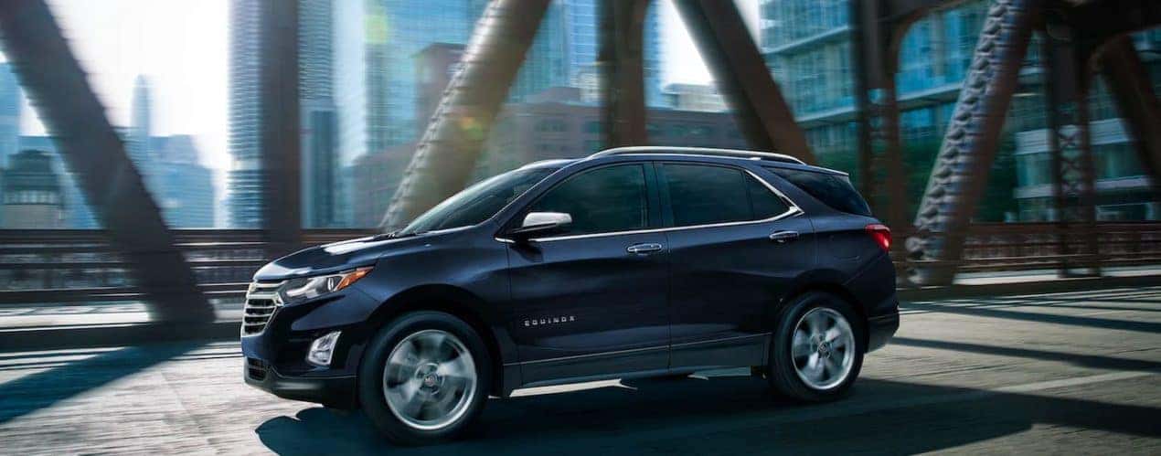 A dark blue 2021 Chevy Equinox is shown from the side driving down a steel bridge in a city after winning the 2021 Chevy Equinox vs 2021 Nissan Rogue battle.