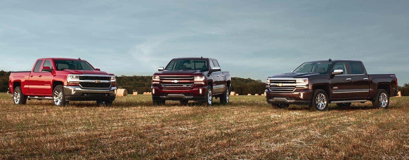 Three red 2016 Chevy Silverado 1500s are parked in a field.