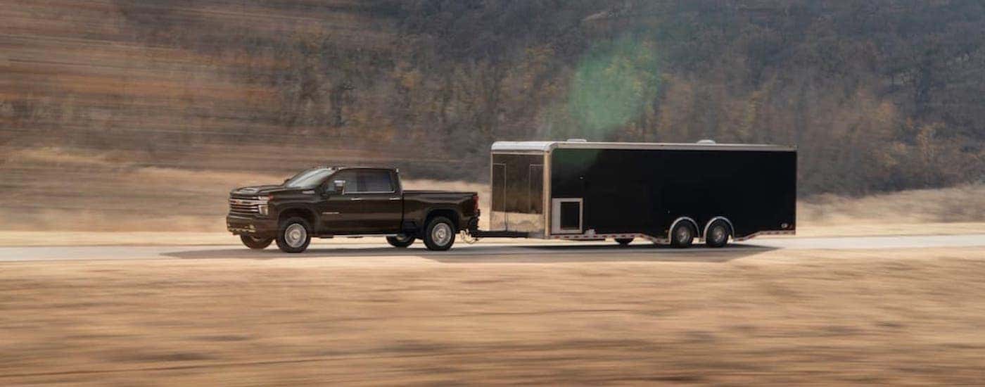 A black 2020 Chevy Silverado 2500HD is towing a black trailer on a desert road.
